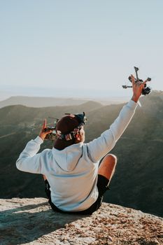 Man with drone and controller enjoying mountain view on a sunny day.